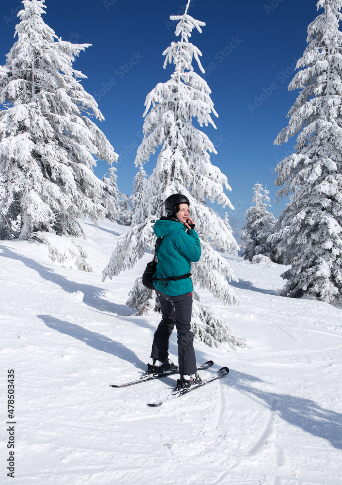 happy woman in a ski suit, helmet, stands in the mountains against the background of ice trees on a sunny winter day. a minute of rest, relaxation, pleasure, winter holidays. love winter