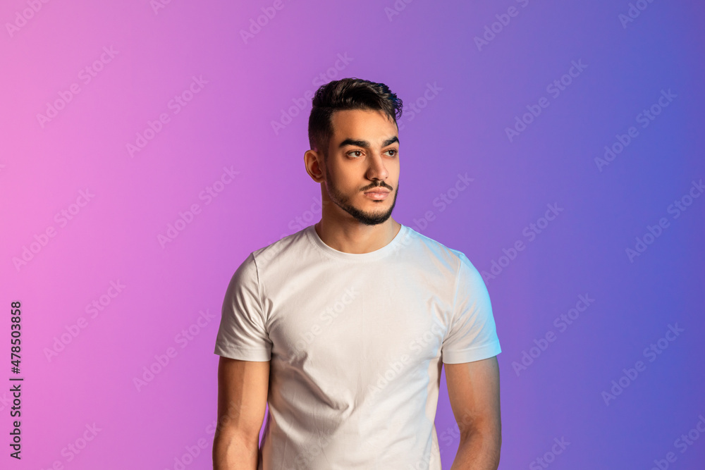 Portrait of serious young Arab man in white t-shirt posing and looking away in neon light Portrait of serious young Arab man in white t-shirt posing and looking away in neon light