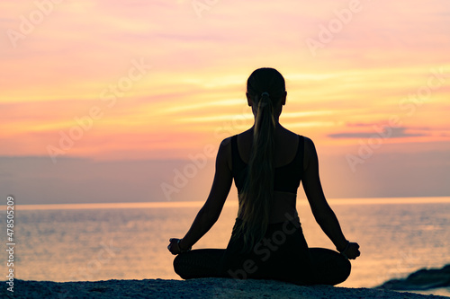 Young woman with long hair meditating on the rock by the sea at colorful sunrise