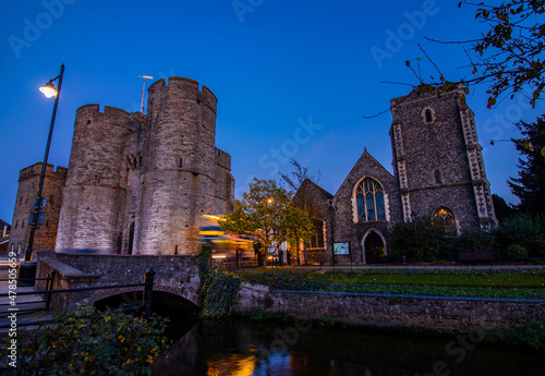 A bus passing by Westgate Towers in Canterbury, with the Great Stour river in the foreground. Night. photo