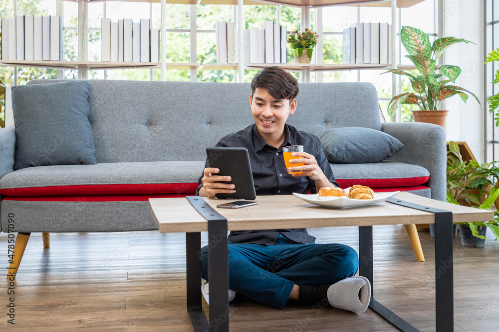 Asian businessman freelance sitting on floor front of sofa using table with meal breakfast. Concept for working at home.