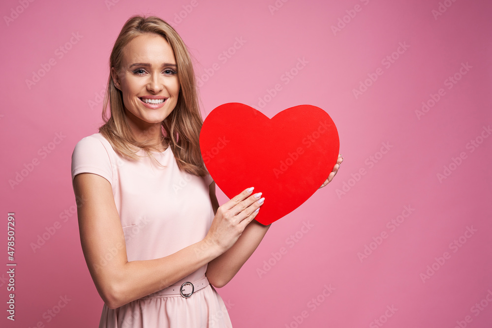 Caucasian ethnicity woman on pink background holding wooden heart Caucasian ethnicity woman on pink background holding wooden heart