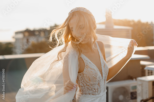 Wind in hair, Young blond bride, wedding makeup, happy. Beautiful woman posing in white wedding dress and bridal veil. Wedding portrait. Bridal fashion model posing on roof. photo