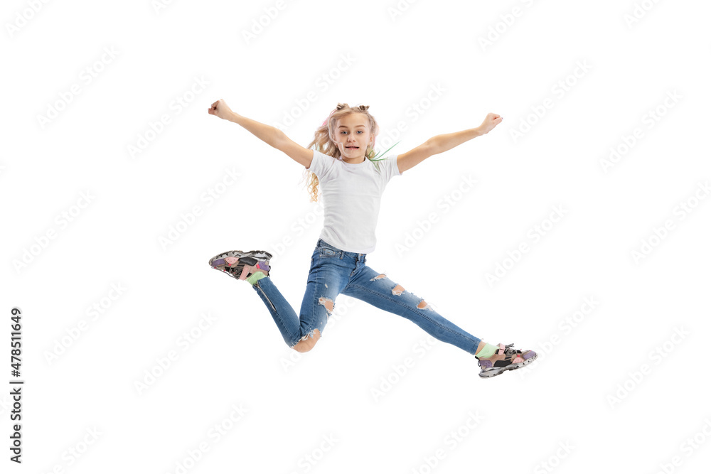 Dynamic portrait of little girl, kid in casual clothes jumping, having fun isolated on white studio background.