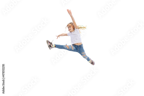 Dynamic portrait of little girl, kid in casual clothes jumping, having fun isolated on white studio background.