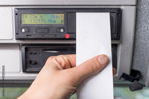 Close up of a driver holding empty printed day shift in focus against a digital tachograph out of focus in background