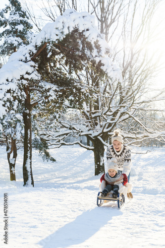 Mother and her cute little son having on a sledding hill during sunny winter day