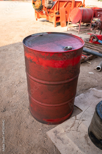 A dirty red chemical or lubricant oil barrel drum which is placed at mechanic workshop in the factory. Industrial object photo.