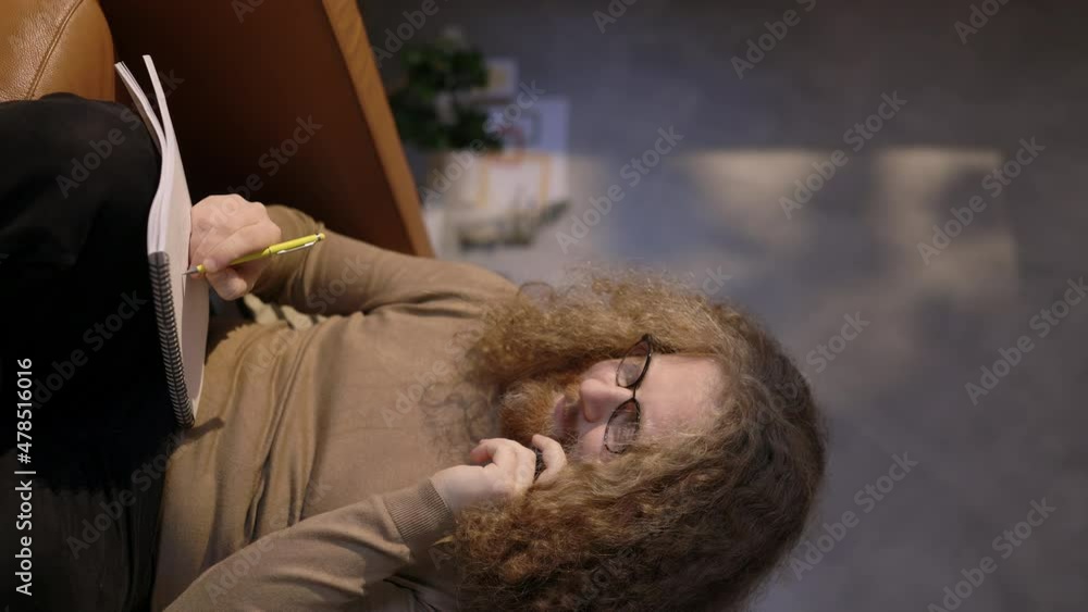 Young Man Working Remotely from Home, Talking on the Phone and Taking Notes sitting on the Sofa in Cozy Living Room, Freelancer Working at Home, Indoor, Copy Space, Vertical Video Format Young Man Working Remotely from Home, Talking on the Phone and Taking Notes sitting on the Sofa in Cozy Living Room, Freelancer Working at Home, Indoor, Copy Space, Vertical Video Format