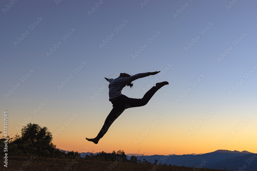 Silhouette of a beautiful girl jumping on mountain park sunset background