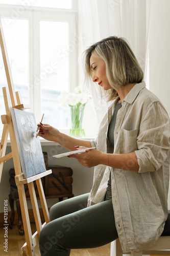 Young woman artist painting on canvas on the easel