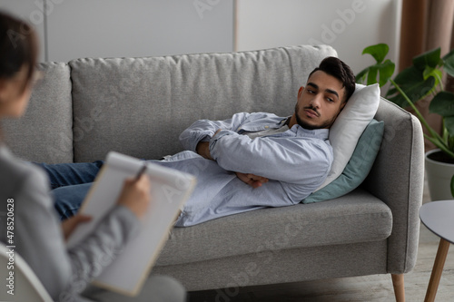 Stress and depression concept. Psychologist working with arab man lying on couch while having session with therapist