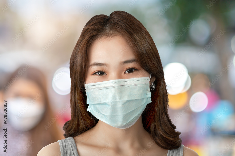 A close-up of a young Asian woman with smile under a sanitary face mask against coronavirus or COVID-19 at a street in an urban city. Virus and illness protection, sanitizer in a public crowded place A close-up of a young Asian woman with smile under a sanitary face mask against coronavirus or COVID-19 at a street in an urban city. Virus and illness protection, sanitizer in a public crowded place