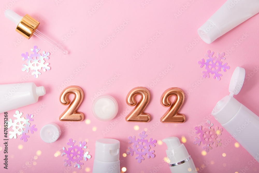 Top view of the cosmetics containers on pink background.Rose gold numbers 2022 and festive bokeh above.Good for new year offer and text overlay. Top view of the cosmetics containers on pink background.Rose gold numbers 2022 and festive bokeh above.Good for new year offer and text overlay.
