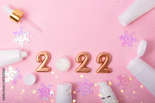 Top view of the cosmetics containers on pink background.Rose gold numbers 2022 and festive bokeh above.Good for new year offer and text overlay.