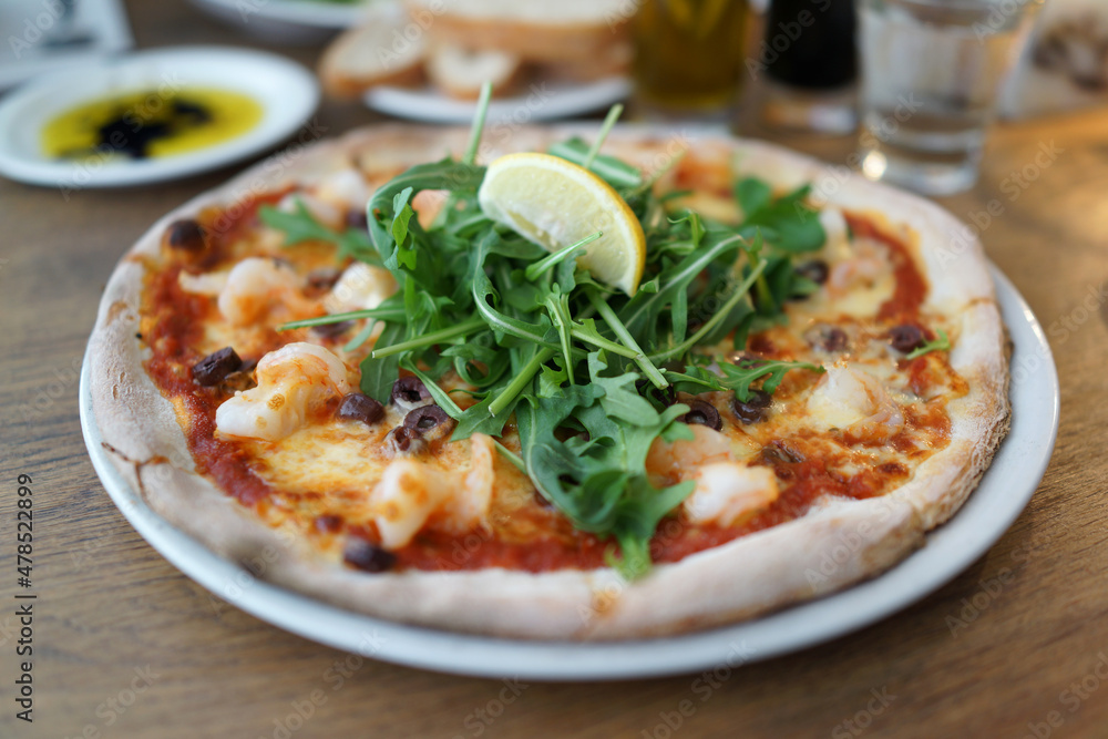 Pizza covered with roquette and shrimps on a plate close up Pizza covered with roquette and shrimps on a plate close up