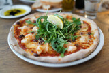 Pizza covered with roquette and shrimps on a plate close up