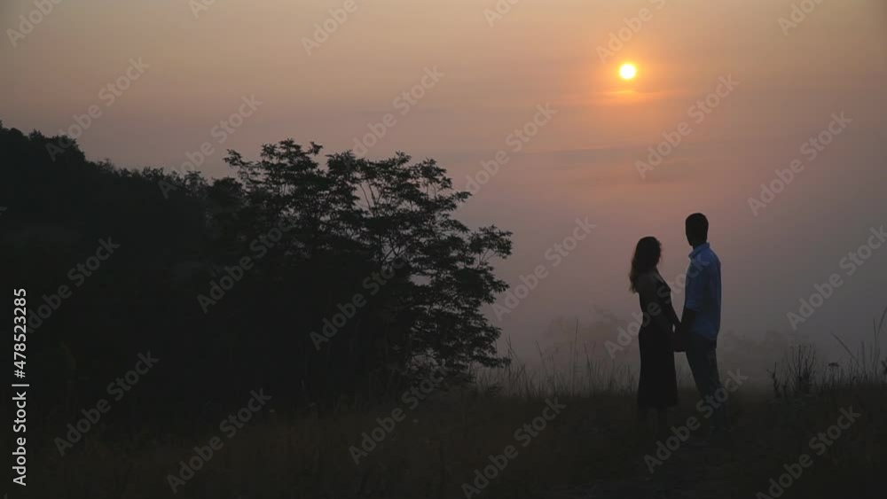 Young man and woman standing and admiring scenic sunset landscape together. Romantic date of two lovers outdoor. Pair enjoying beautiful moment at nature. Romance and happiness concept. Slow motion Young man and woman standing and admiring scenic sunset landscape together. Romantic date of two lovers outdoor. Pair enjoying beautiful moment at nature. Romance and happiness concept. Slow motion