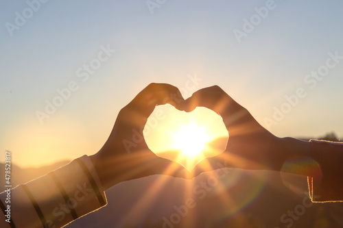 Silhouette hands in heart shape on mountain outdoors in summer park at sunset
