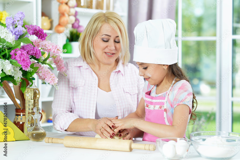 Cute girl in white hat with her mother making dough Cute girl in white hat with her mother making dough