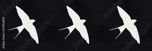 Black background like canvas fabric with silhouette of a white swallows. Folk background with birds motif.  