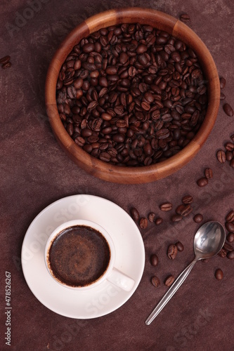 Coffee beans in a wooden plate and a cup of brewed coffee on a brown background
