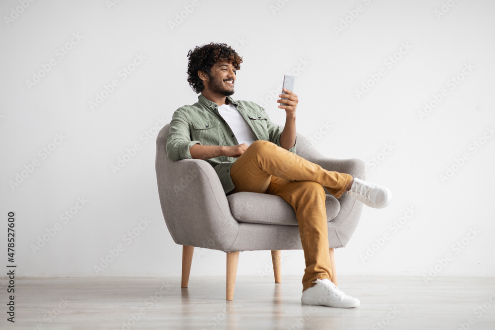 Cheerful young indian man chatting with girlfriend, using smartphone