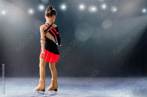 Little skater rides on rings in red and black dress on ice arena