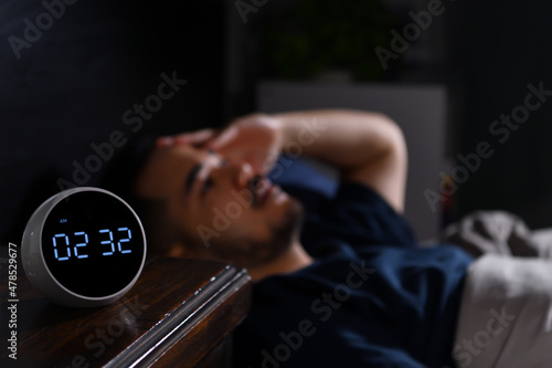 Depressed young Asian man lying in bed cannot sleep from insomnia. focus on clock