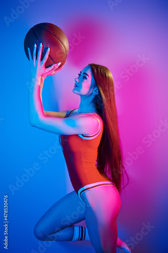 Holds ball. Fashionable young woman standing in the studio with neon light