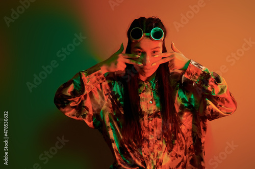 Retro eyewear. Fashionable young woman standing in the studio with neon light