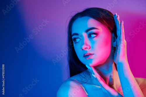 Neutral facial expression. Fashionable young woman standing in the studio with neon light © standret