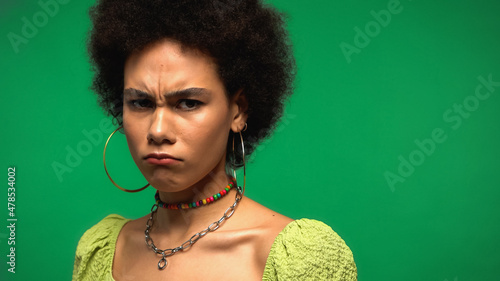 frustrated african american woman frowning and looking at camera isolated on green photo