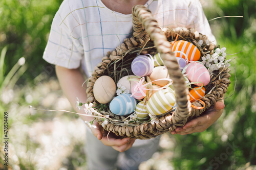 Easter egg hunt in spring garden. Funny boy with eggs basket and bunny ears on Easter egg hunt in sunny spring garden. Children celebrating Easter. Happy easter card