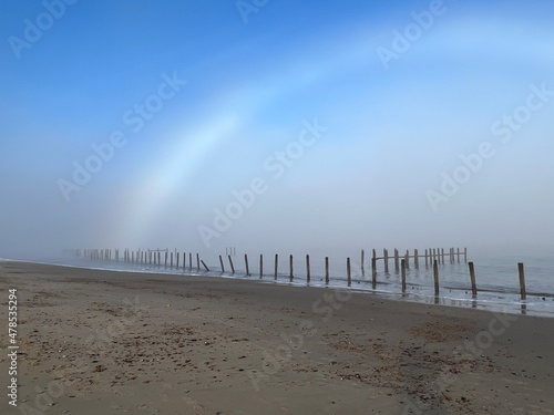 Beautiful beach landscape tranquil scene with fogbow over sandy shore by ocean at Happisburgh in Norfolk coast in East Anglia uk with blue skies after foggy mist cold morning in December photo