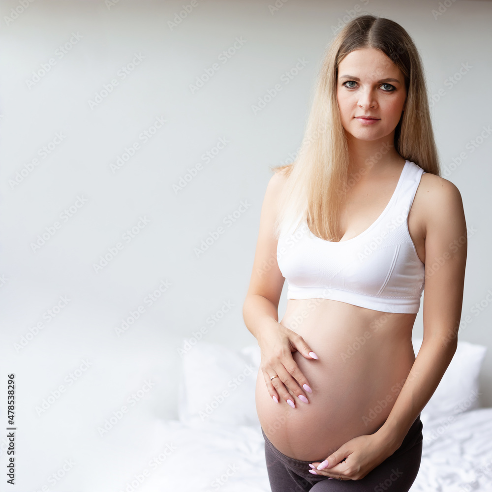 Cute pregnant blonde on a light background. Looks into the camera. Portrait. Background. Photo square. Copyspase Cute pregnant blonde on a light background. Looks into the camera. Portrait. Background. Photo square. Copyspase