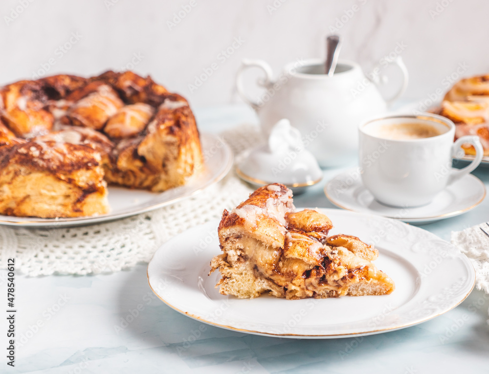 Portion of homemade cinnamon rolls on a white plate on a white table with coffee and pastry buns for breakfast. Traditional Swedish and Danish recipe. Portion of homemade cinnamon rolls on a white plate on a white table with coffee and pastry buns for breakfast. Traditional Swedish and Danish recipe.
