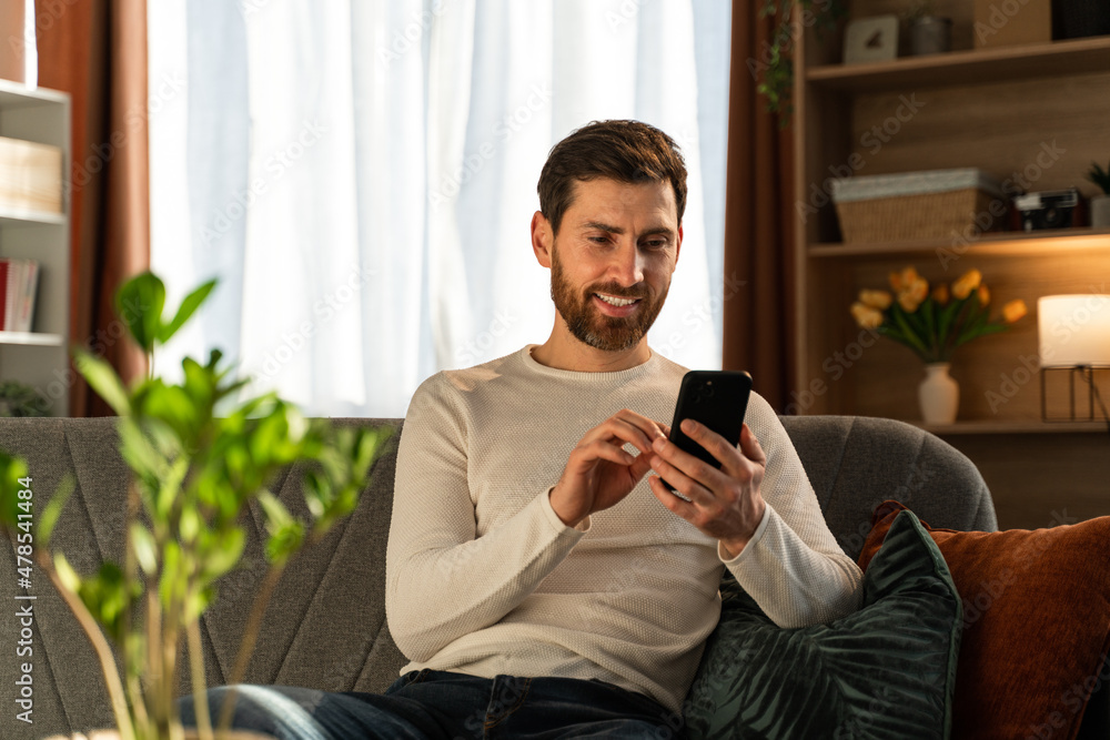 Happy youthful businessman making freelance work at his room and typing messages at the smartphone