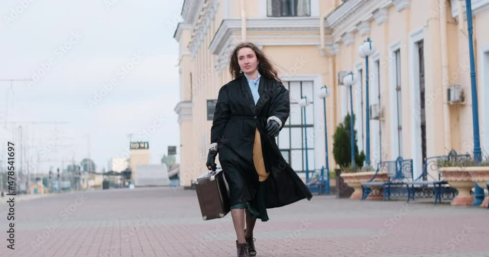 Young woman with leather bag walks through the city. Girl in raincoat with suitcase in her hands walks confidently with confident gait Young woman with leather bag walks through the city. Girl in raincoat with suitcase in her hands walks confidently with confident gait