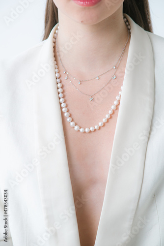 Trending silver necklace with pearls on a beautiful young girl in a white fashionable jacket. Beauty and fashion 