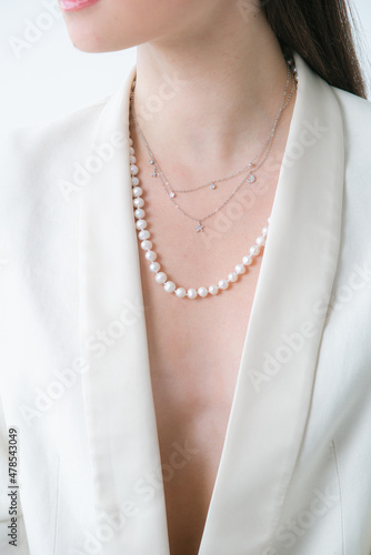 Trending silver necklace with pearls on a beautiful young girl in a white fashionable jacket. Beauty and fashion 