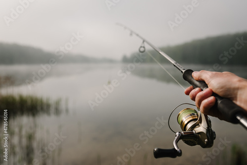 Fishing day. Fisherman with rod, spinning reel on river bank. Fishing for pike, perch, carp. Fog against the backdrop of lake. Background misty morning. wild nature. The concept of a rural getaway.