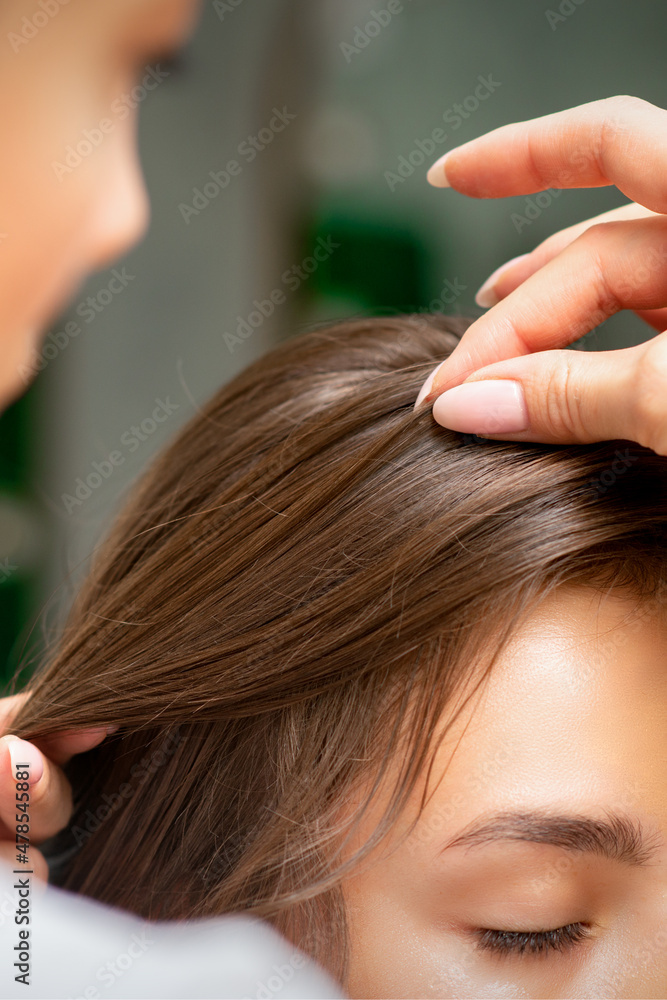 Obraz premium A hairdresser is making the hairstyle of a young brunette woman in a hair salon, close up