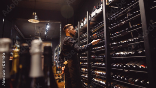 Sommelier Bartender man at wine shop full of bottles with alcohol drinks photo