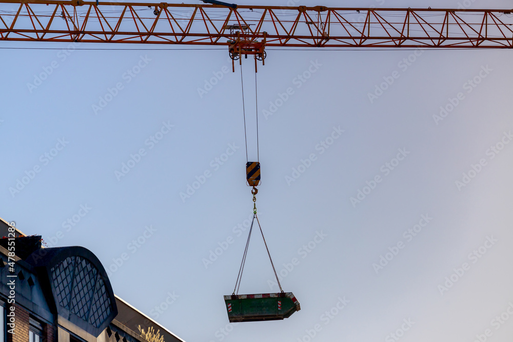 Build and structure concept, Yellow crane with cable or sling in the construction site work lifting construction equipment on the top of high building with blue clear sky as background.