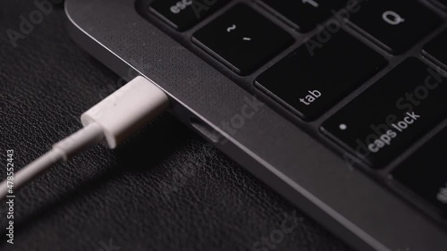 Male hand plugging in a white power USB-C or Type C Cable into a laptop computer's USB-C port. UHD