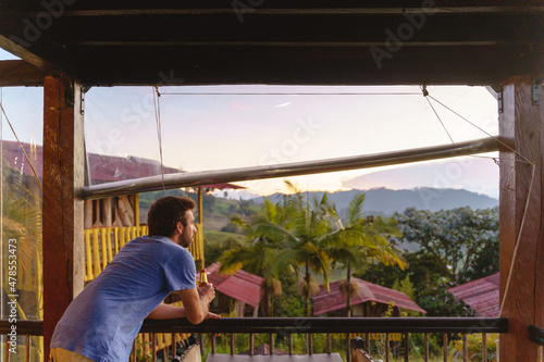 Horizontal side view of latin man drinking beer sightseeing from viewpoint valley background. Horizontal view of man sightseeing at sunset in Colombia. People and travel destination in South America