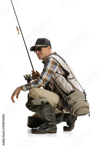 Portrait of young man, professional fisherman with fishing rod, spinning and equipment sitting isolated over white studio background