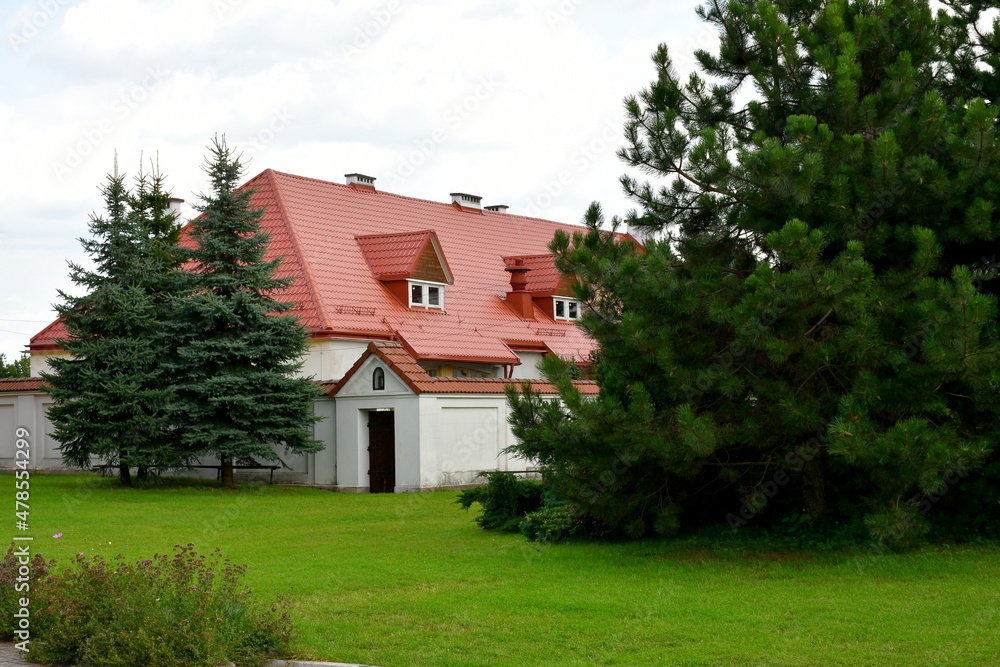 A view of the entrance to an old abandoned monastery located behind a concrete gate with a small roof located at the end of a well maintained lawn with some trees growing within its scope in Poland A view of the entrance to an old abandoned monastery located behind a concrete gate with a small roof located at the end of a well maintained lawn with some trees growing within its scope in Poland