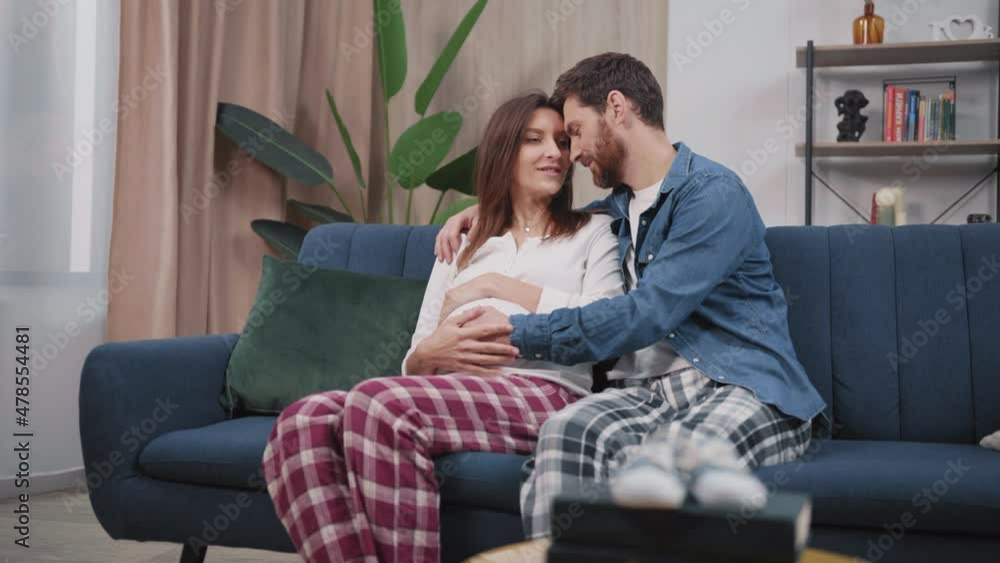Family life moments. Cheerful husband with pregnant wife sitting on couch, sharing future plans and enjoying each other. Relationship. Pregnancy. Family life moments. Cheerful husband with pregnant wife sitting on couch, sharing future plans and enjoying each other. Relationship. Pregnancy.